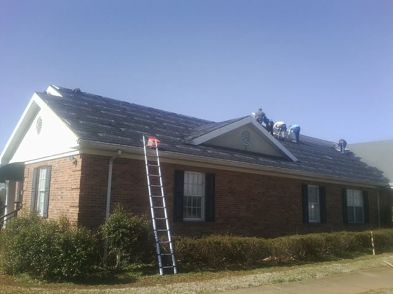 Crew tearing shingles off a brick ranch roof with a ladder set — Metal Roof Repair work by our crew in Ontario