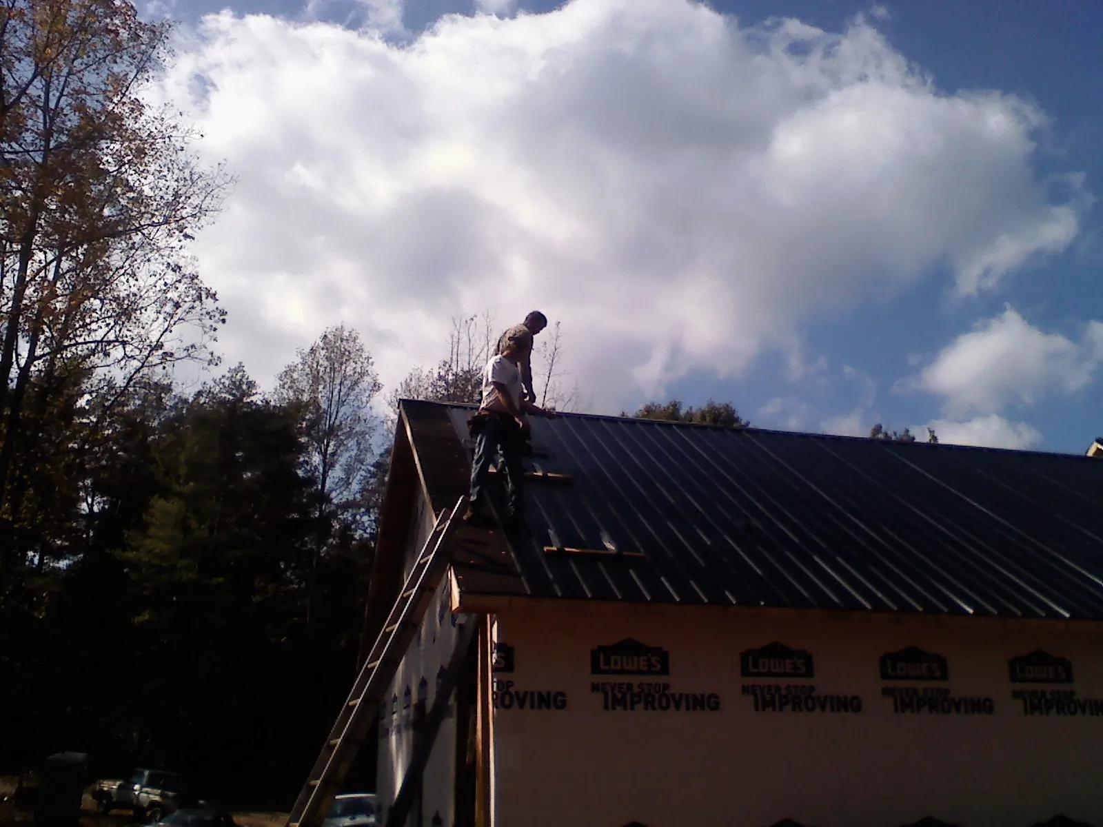 Roofer fastening dark metal panels high against a cloudy sky, from a Roof Inspection job in Ontario