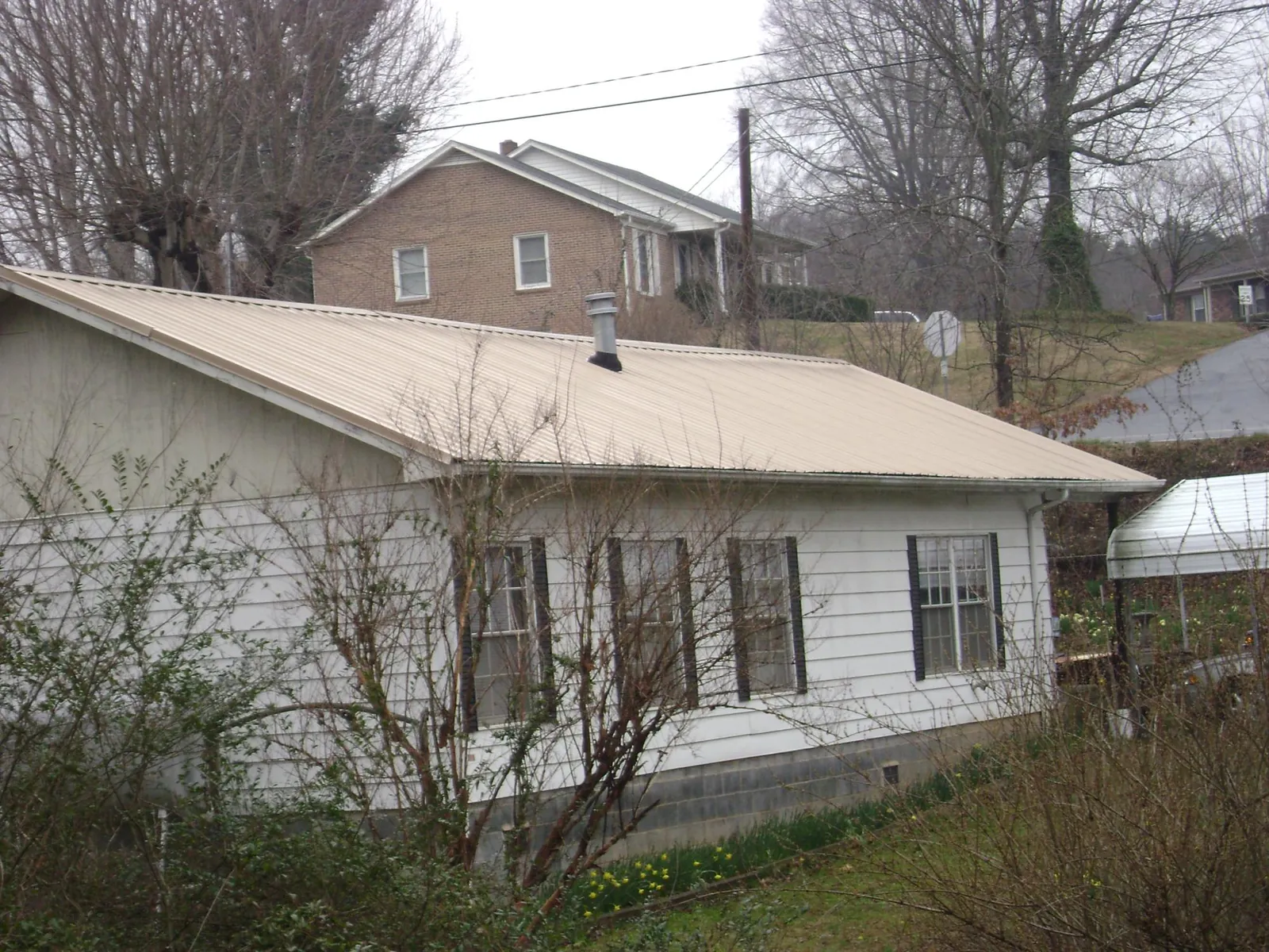 Tan metal roof on a white sided house set into a hillside — Commercial Roofing by Roofing Brothers in Ontario
